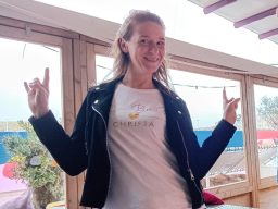 Christa met een witte T-shirt en zwarte leren jas, maakt rockhandgebaren.