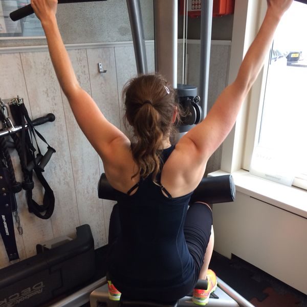 Christa in sportoutfit voert oefening uit op een fitnessapparaat.