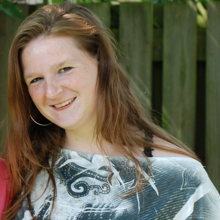 Christa met lange, golvende haren en een glimlach, gekleed in een zwart-wit shirt.