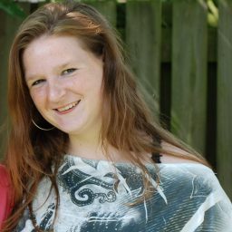 Christa met lange, golvende haren en een glimlach, gekleed in een zwart-wit shirt.
