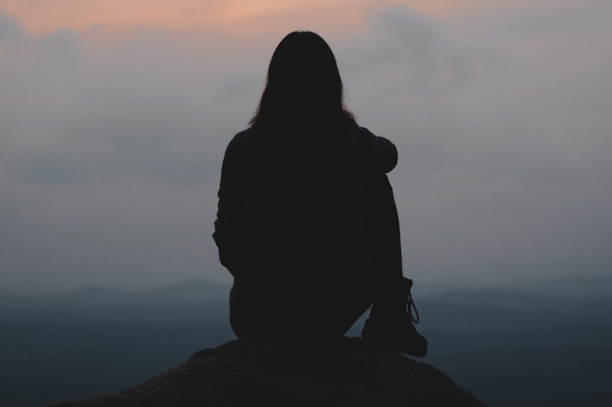 Vrouw zit op een rots en kijkt uit over een bergachtig landschap.