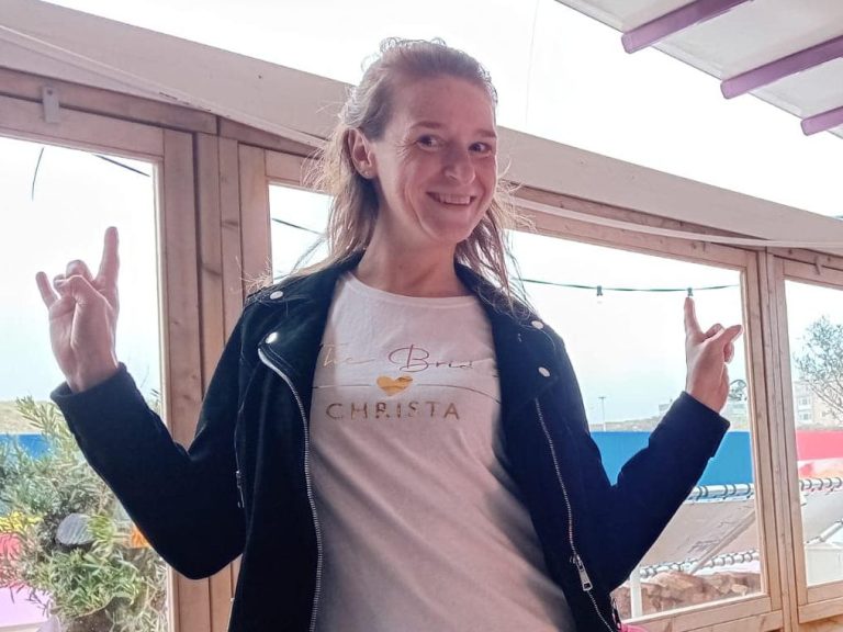 Christa met een witte T-shirt en zwarte leren jas, maakt rockhandgebaren.