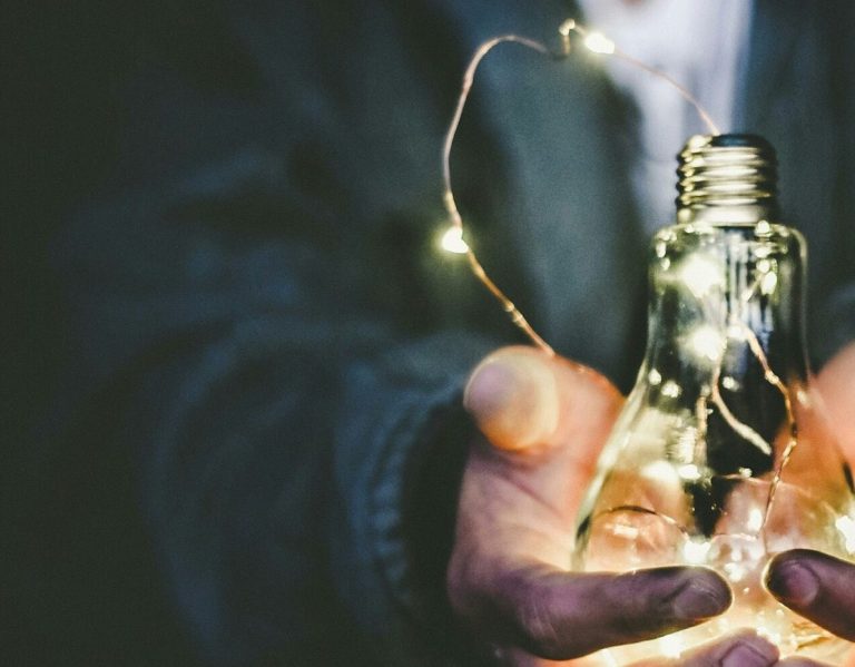 Een hand houdt een gloeilamp vol met warme, sprankelende lichtjes.