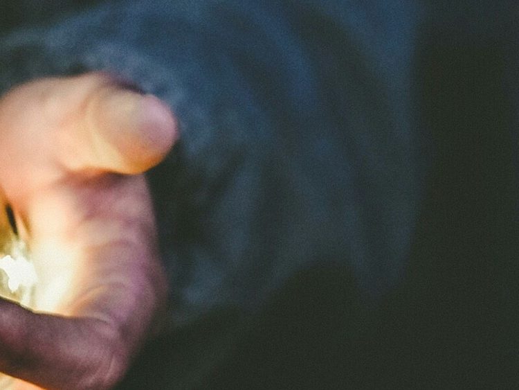 Een hand houdt een kleine lichtbron vast in de duisternis.