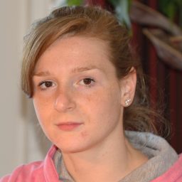 Christa met een roze hoodie en een neutrale gezichtsuitdrukking.